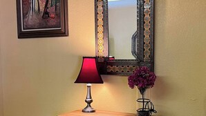 Un mueble de madera color turquesa con cajones, una lámpara roja y un florero con flores moradas encima.