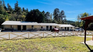 Un motel con una estructura de dos pisos, un área de estacionamiento techada y un patio delantero cercado.