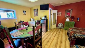 Habitación compacta con mesa de comedor, sillas, cama, kitchenette pequeña y televisión.