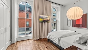 Ein Schlafzimmer mit großem Fenster, einem Bett, einem Flachbildfernseher und einer modernen Pendelleuchte.