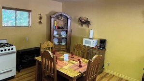 Un comedor con una mesa de madera, cuatro sillas, un mueble empotrado de madera con vajilla, un microondas y una estufa a gas.