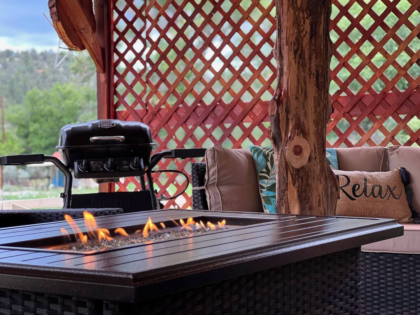 A barbecue grill with a built-in fire feature, a wicker table, and a red lattice backdrop.