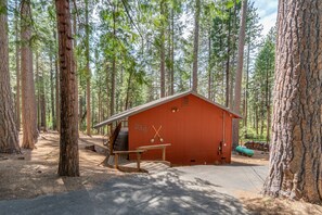 A red cabin with a wooden deck and two crossed paddles on the door, surrounded by tall trees. - A/C, Pet Friendly/ 3BR + Rec Room in Blue Lake Springs (Arnold)