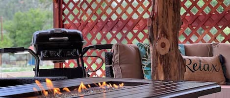Een barbecue met geïntegreerde vuurplaats, een rieten tafel en een rode, open haag.