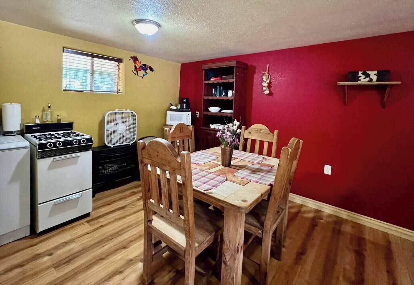 Cocina compacta con sillas de madera, una mesa de comedor, estufa y ventilador.