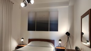 Ein Schlafzimmer mit Bett, Nachttischen, einem Spiegel und einem Fenster mit Vorhängen.