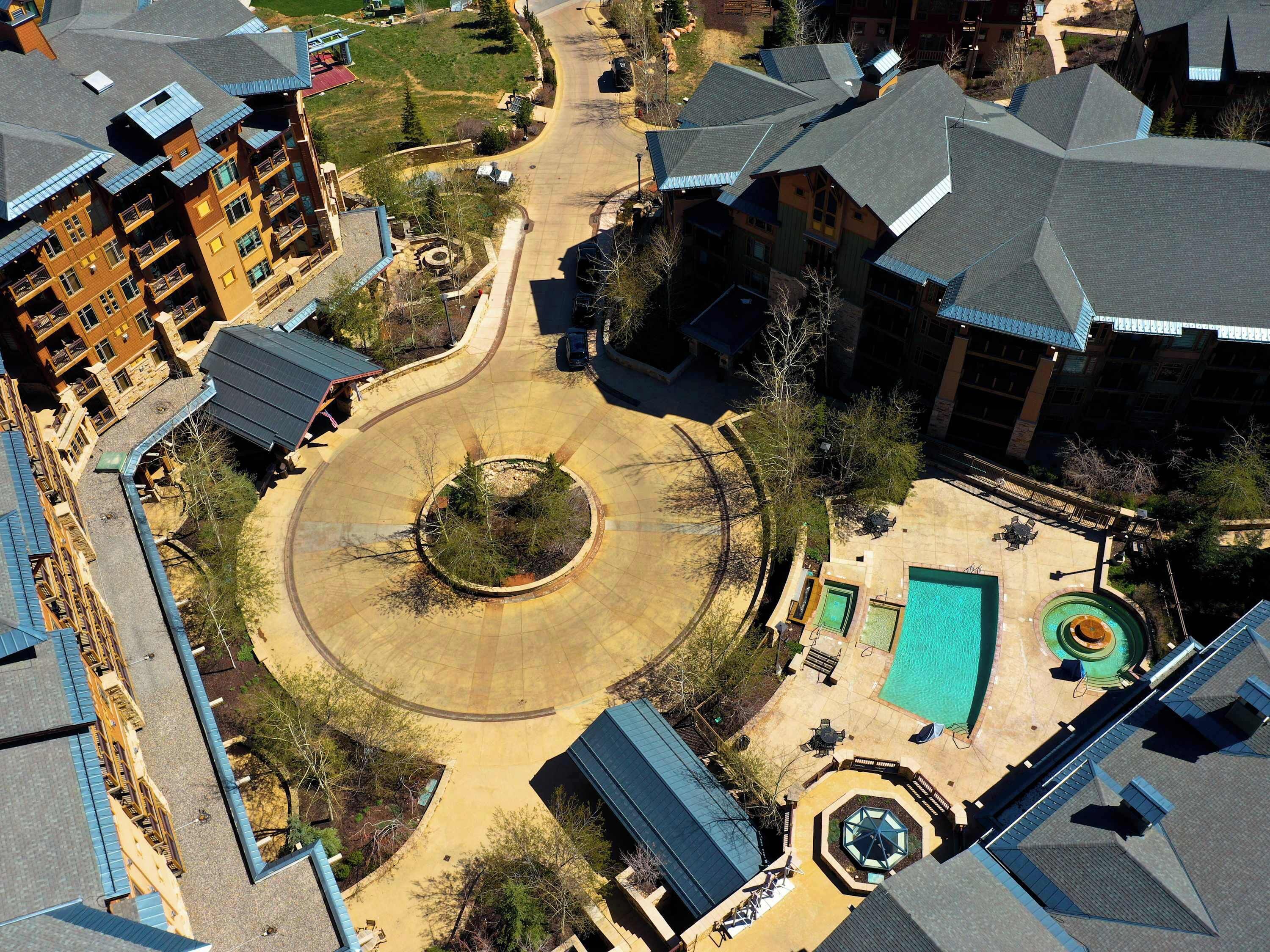 An aerial view of a residential area with a circular driveway, a swimming pool, and multiple buildings with balconies.