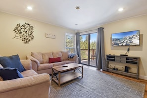 Relax in this stylish living room with a sofa, flat-screen TV, and sliding glass door leading to an outdoor deck.