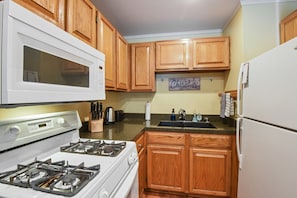 Kitchen area with microwave, stove, refrigerator, sink, and countertop with a knife block and kettle.