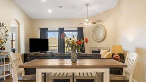 Ein Essbereich mit Holztisch und Stühlen, einer Couch, einem Fernseher und einer Vase mit Blumen.