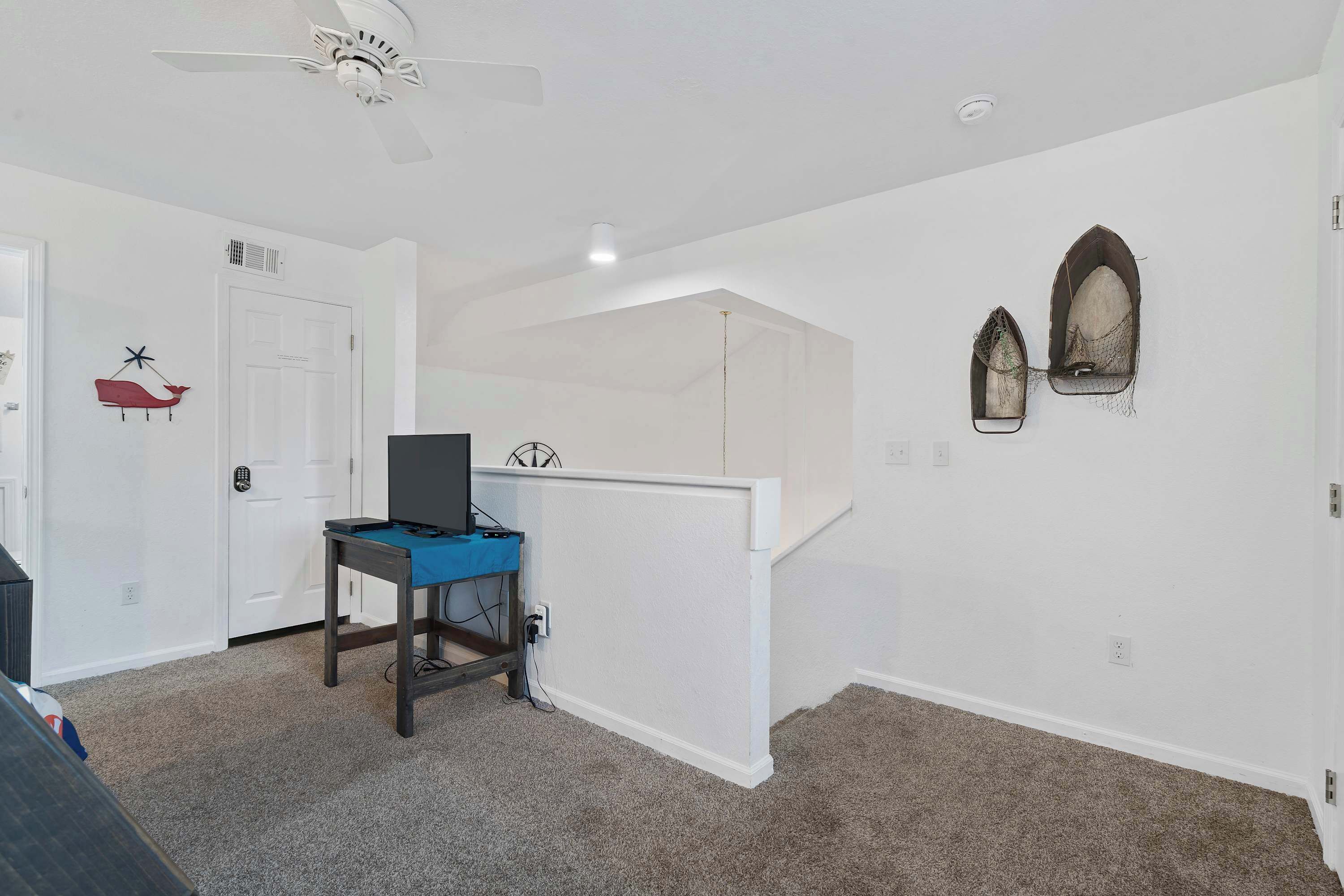 A room with a white ceiling fan, a white door, a blue table with a computer, and two wall-mounted decorative items.