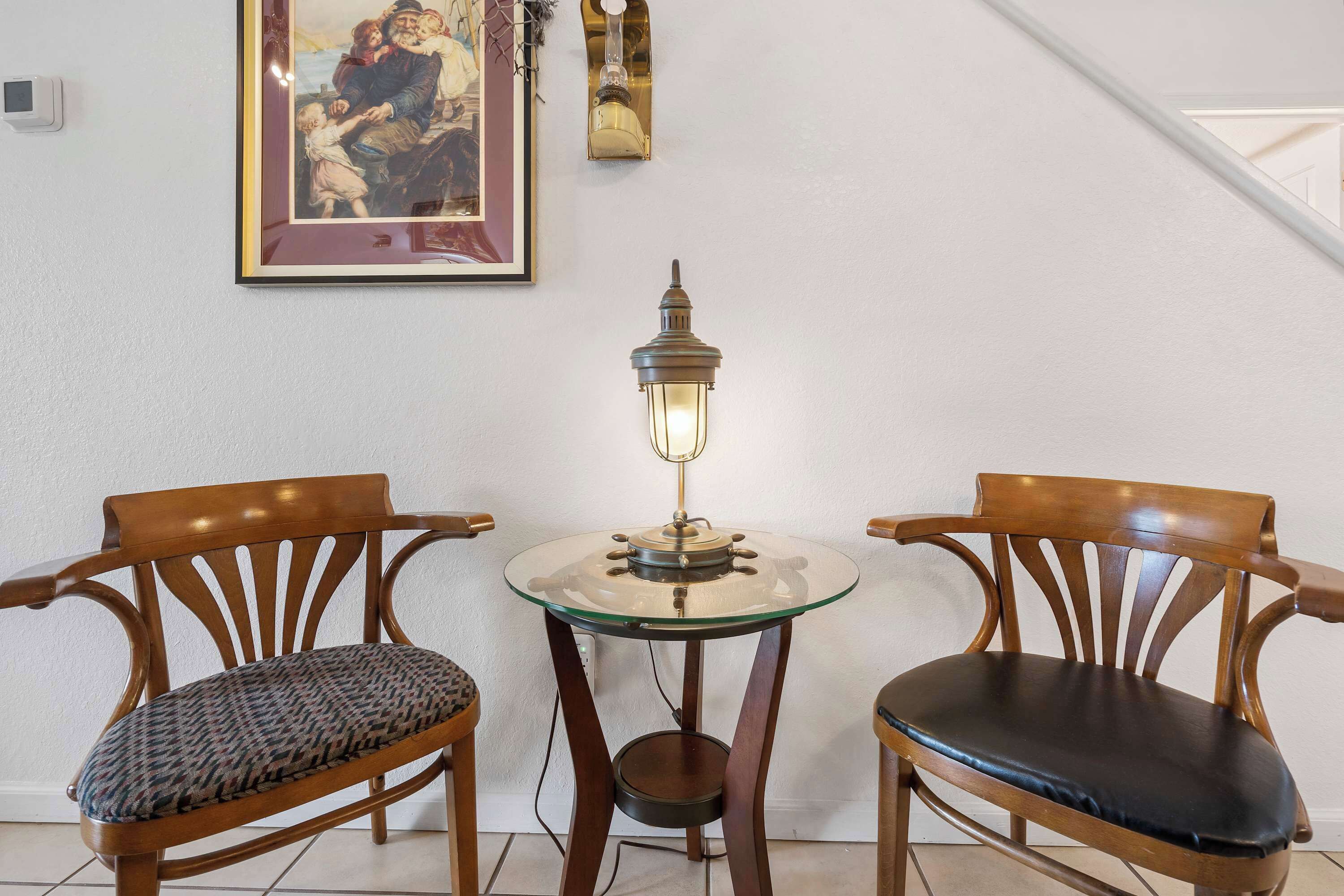 A dining area with two wooden chairs, a glass table, and a wall-mounted lamp.