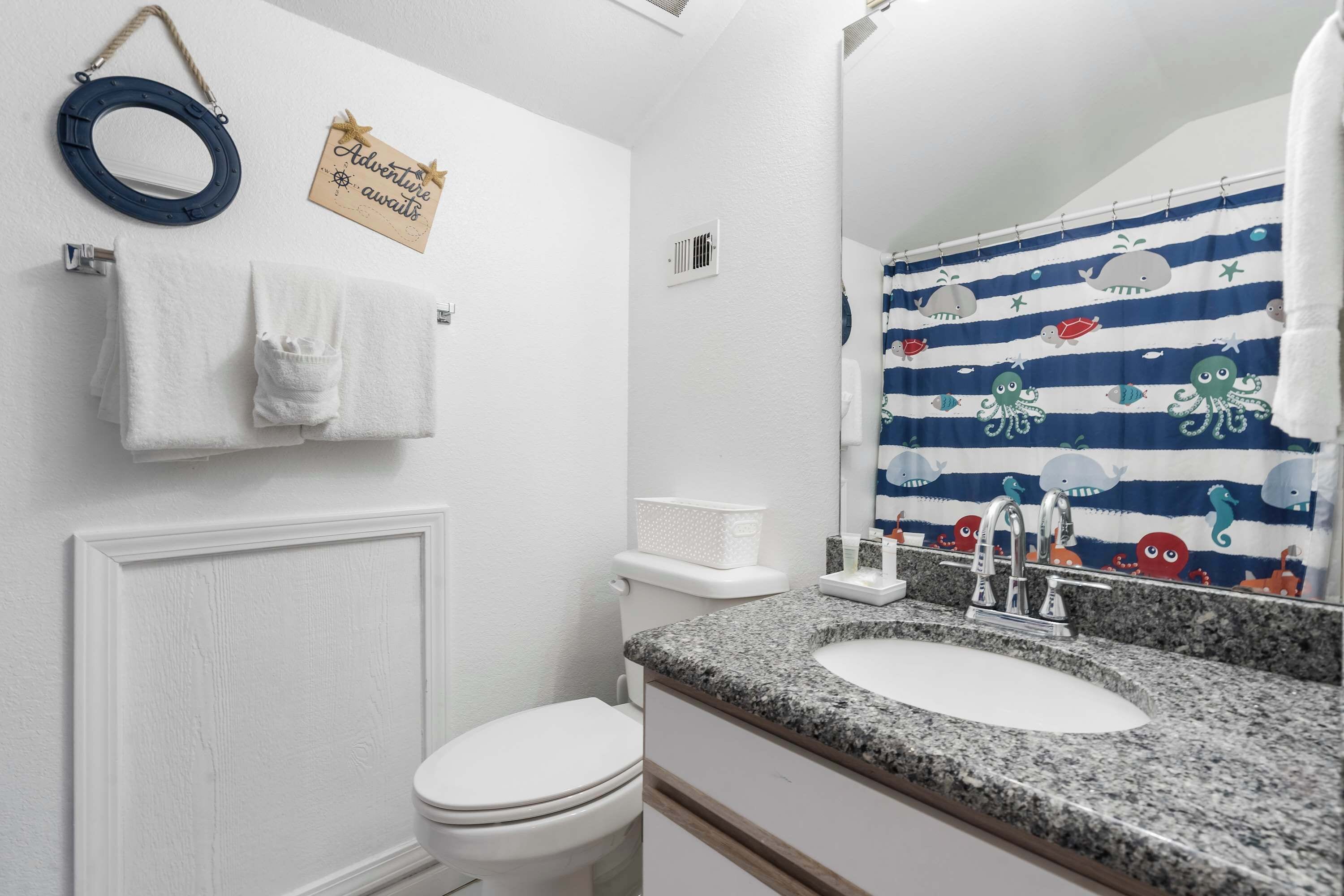 Ein Badezimmer mit einer weißen Toilette, einem Granitwaschbecken, einem Spiegel und einem duschvorhang mit blauen Streifen.