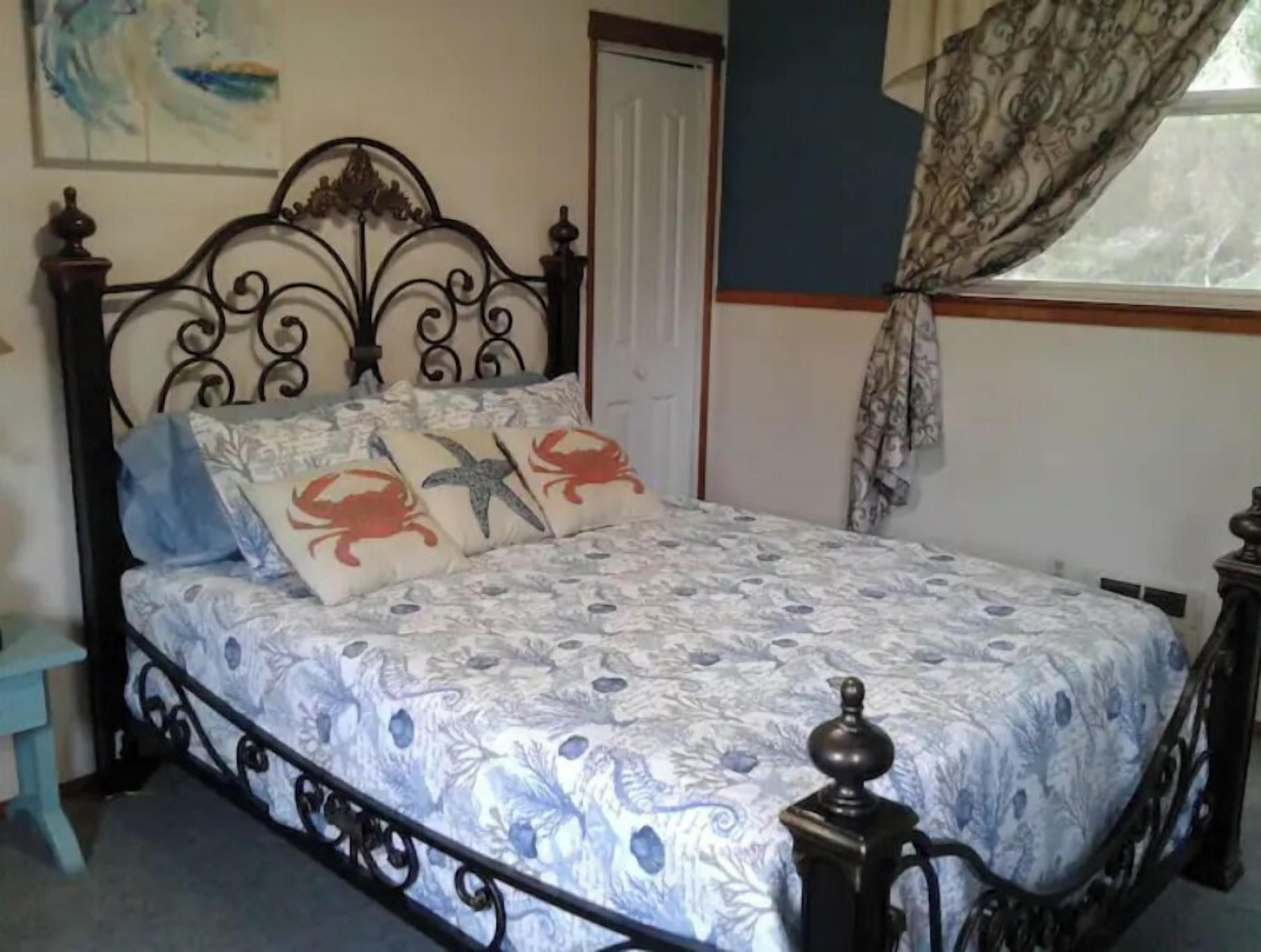 Una cama con una colcha estampada, un cabecero con diseño decorativo y una ventana con cortinas.