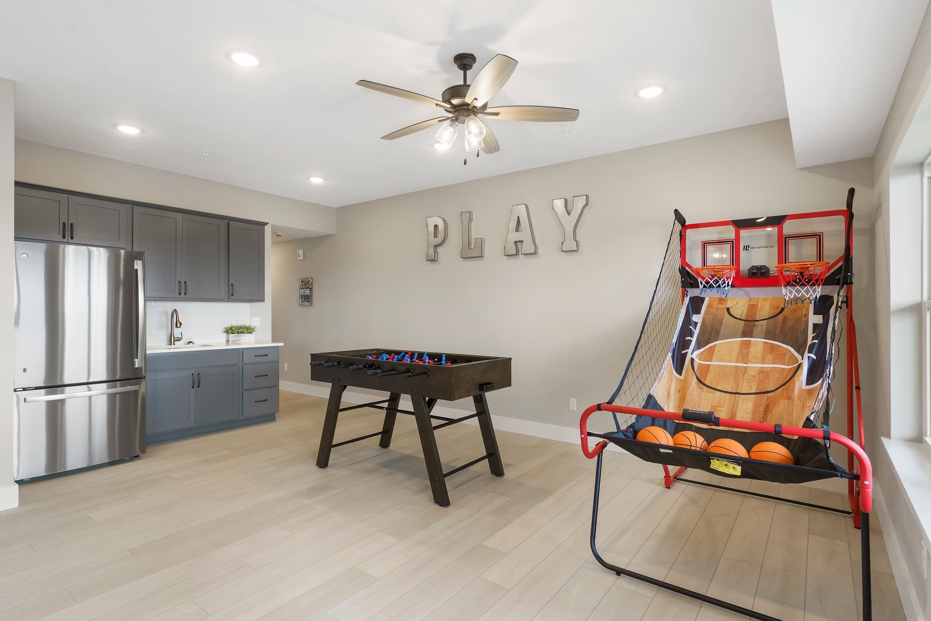 A modern kitchen with grey cabinets, a stainless steel refrigerator, and a foosball table.