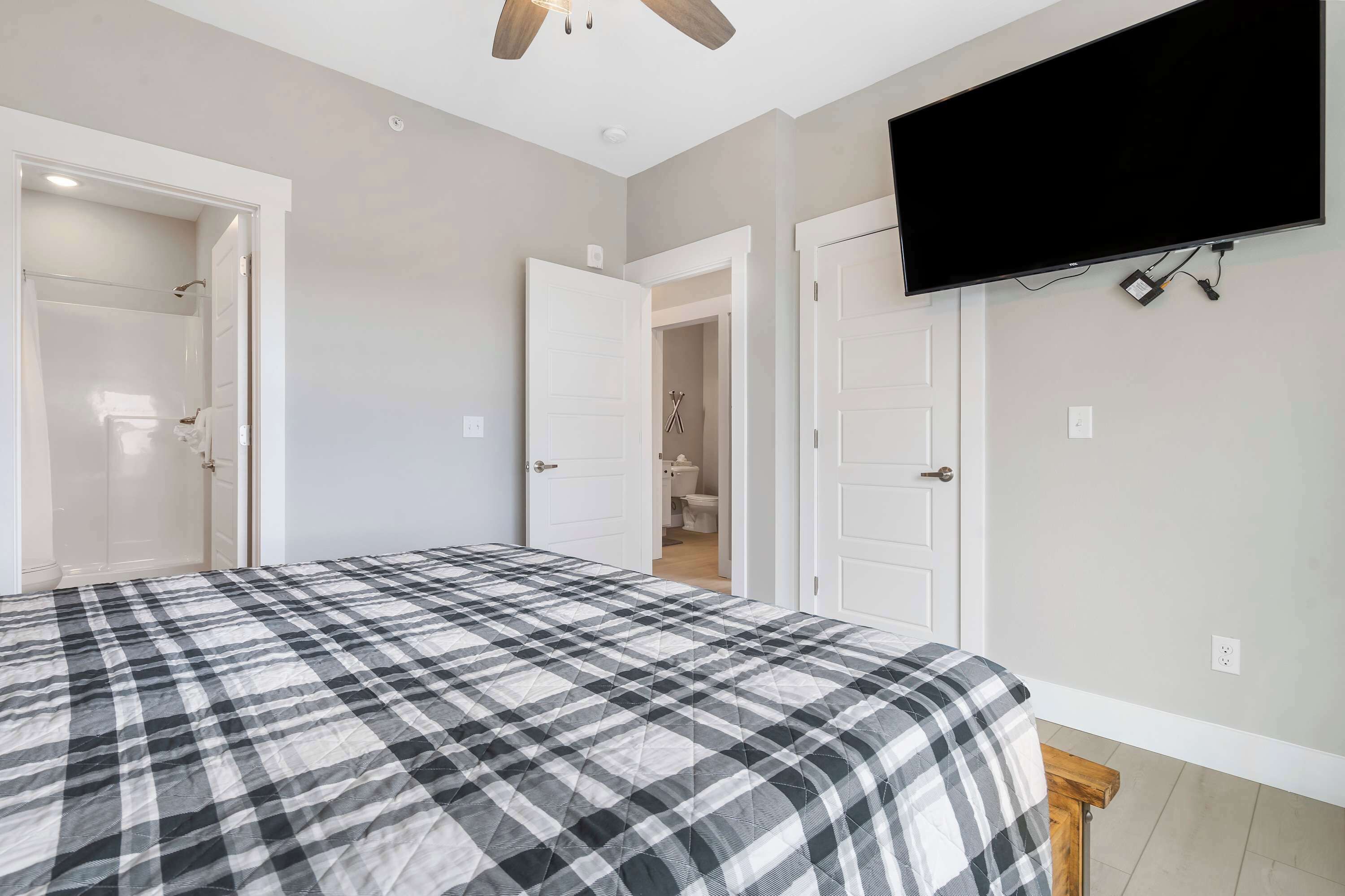 A bedroom with a bed, a TV mounted on the wall, and a bathroom visible through an open door.