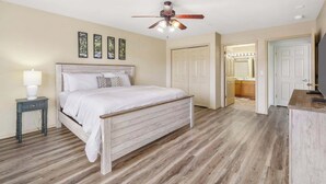 A bedroom with a wooden bed, a nightstand, a ceiling fan, and a view into the kitchen. - Retreat at Par Lane - Family Friendly Condo (Branson West)