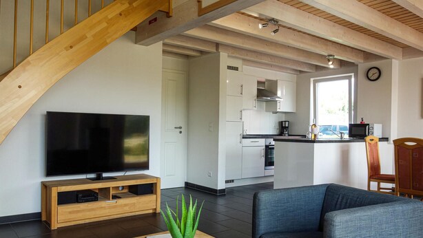 A modern living space with a TV on a wooden stand, a sofa, a coffee table with a plant, and a kitchen area with white cabinets and appliances. - Beautiful home in Nordhorn with kitchen (Nordhorn)