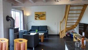 A living room with a sofa, chairs, a coffee table, a fireplace, a painting on the wall, and a wooden staircase. - Beautiful home in Nordhorn with kitchen (Nordhorn)