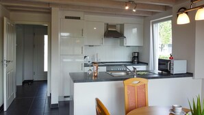 A modern kitchen with white cabinets, a stainless steel range hood, a built-in oven, a sink, and a microwave. There is a dining area with a wooden table and chairs. - Beautiful home in Nordhorn with kitchen (Nordhorn)