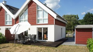 A two-story house with a red exterior, white trim, and a covered patio with outdoor furniture. - Beautiful home in Nordhorn with kitchen (Nordhorn)