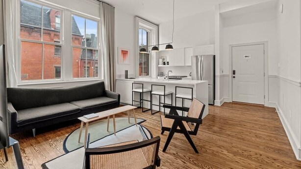 A modern living room with a sofa, a glass coffee table, and a dining area with chairs. - Luxury 1BD Rittenhouse Sq. | Hosted By Stay Rafa (Philadelphia)