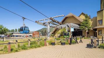 A ski lift station with a cable car and a gondola, a paved area with a fence, and buildings in the background.