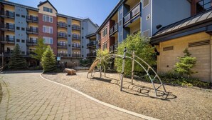 Un patio con un parque infantil, un banco de piedra y un edificio con varios balcones.