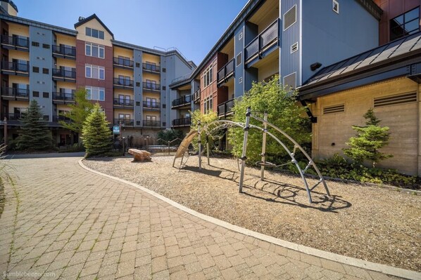 A courtyard with a playground, a stone bench, and a building with multiple balconies.