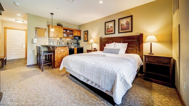 A bedroom with a large bed, a desk, and a kitchenette.