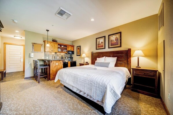 A bedroom with a large bed, a desk, and a kitchenette. - Silver Mtn Studio Condo Ski - Mtn Bike- Hiking (Kellogg)