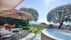 En udendørs terrasse med jacuzzi, træmøbler og havudsigt.