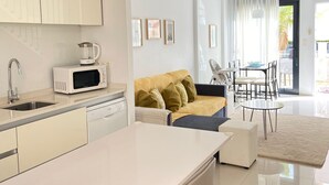 Eine moderne Küche mit weißen Schränken, einer Mikrowelle und einem Spülbecken. Es gibt einen Essbereich mit Tisch und Stühlen, sowie eine Couch mit Kissen.