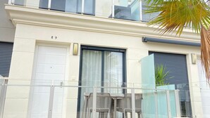 Ein modernes, zweistöckiges Gebäude mit Balkon, Garagentor und einer kleinen Außenbereich-Sitzgelegenheit mit Stühlen.