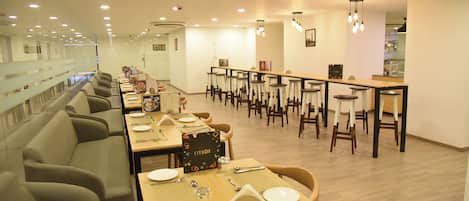 Un restaurante moderno con mesas comunes largas y cabinas, bien iluminado con luces de techo y un diseño limpio y minimalista.