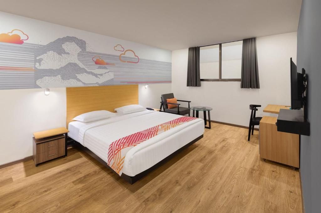 A hotel room with a bed, a desk, a chair, a TV, and a small table.