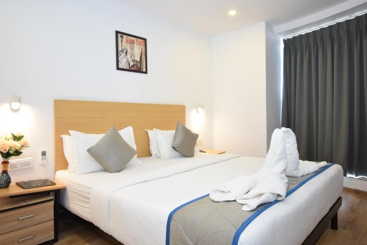A hotel room with a large bed, a wooden headboard, a nightstand with a vase of flowers, and a framed picture on the wall.