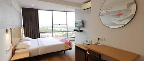 Habitación de hotel con cama, escritorio, silla, televisor y ventana grande con vistas.