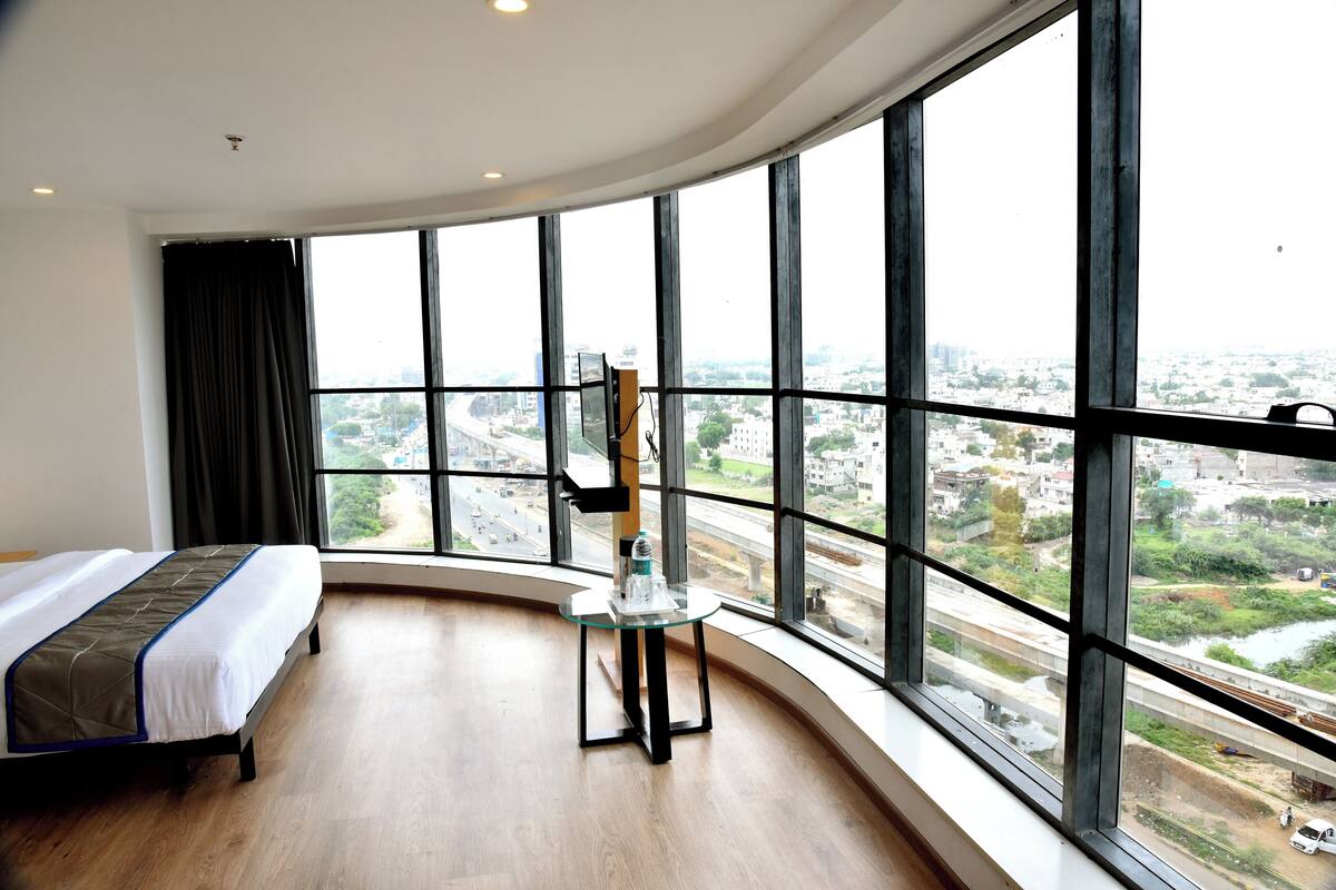 A hotel room with a large curved window offering a view of a cityscape and a highway.