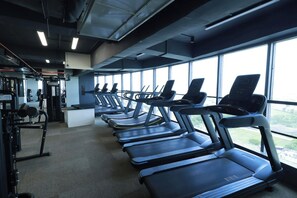 Un gimnasio con varias cintas de correr alineadas en filas, ventanas amplias y equipo de ejercicio.