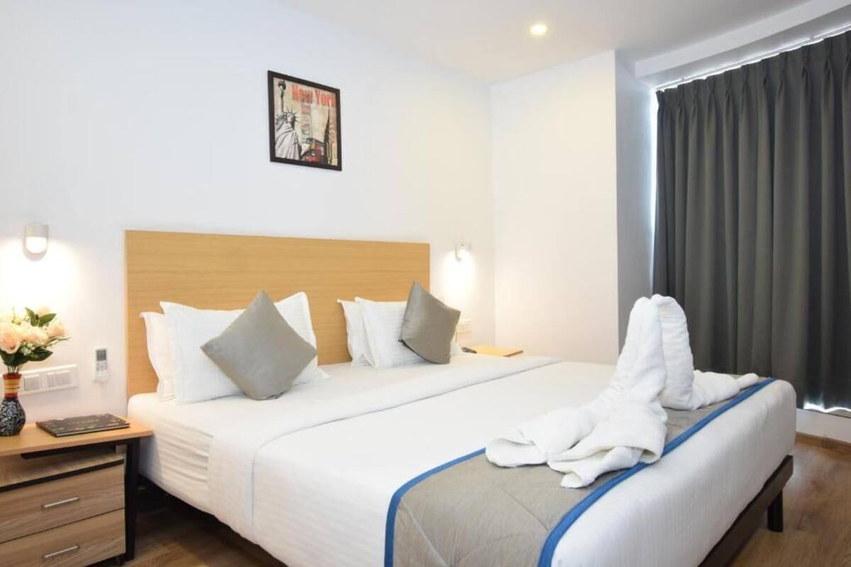 A hotel room with a large bed, a wooden headboard, a nightstand with a vase of flowers, and a framed picture on the wall.