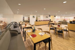 A modern dining area with multiple tables and chairs, a kitchen in the background, and a patterned wall. - Ginger Ahmedabad Rto Circle (Ahmedabad)