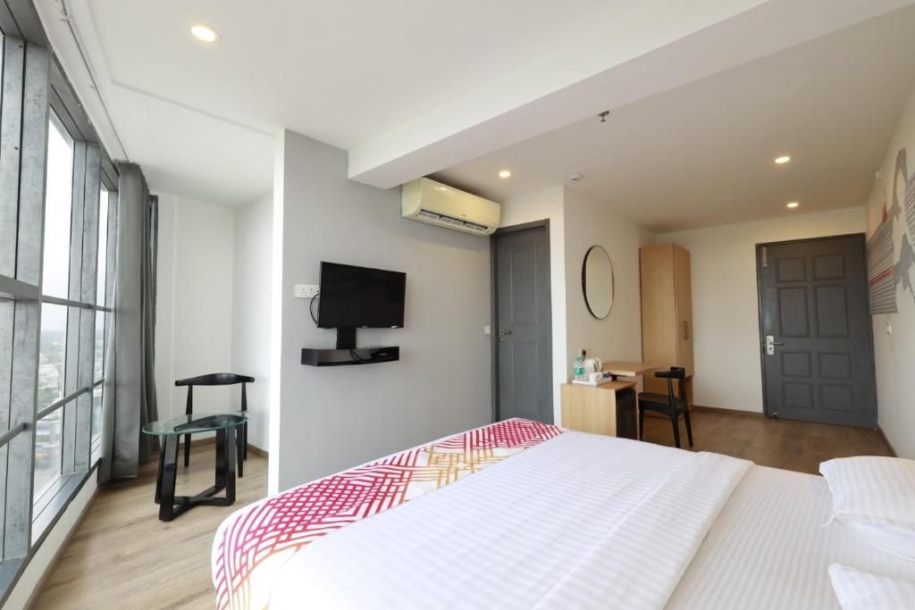 Una habitación de hotel moderna con una cama grande, un escritorio, un televisor y un ventanal con vistas.