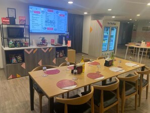 A conference room with a long table, chairs, a screen displaying a menu, and a refrigerator labeled "On The Run". - Ginger Ahmedabad Rto Circle (Ahmedabad)