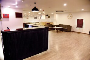 Een moderne hotellobby met een receptiebalie, een zithoek en een klok aan de muur.
