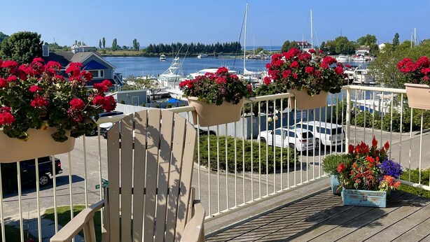 Une terrasse dotée d’une chaise en bois et d’une petite table, offrant une vue sur une marina avec des bateaux et un ciel bleu dégagé.