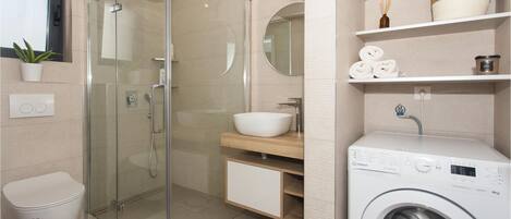 A modern bathroom with a glass-enclosed shower, a sink, and a built-in washing machine.