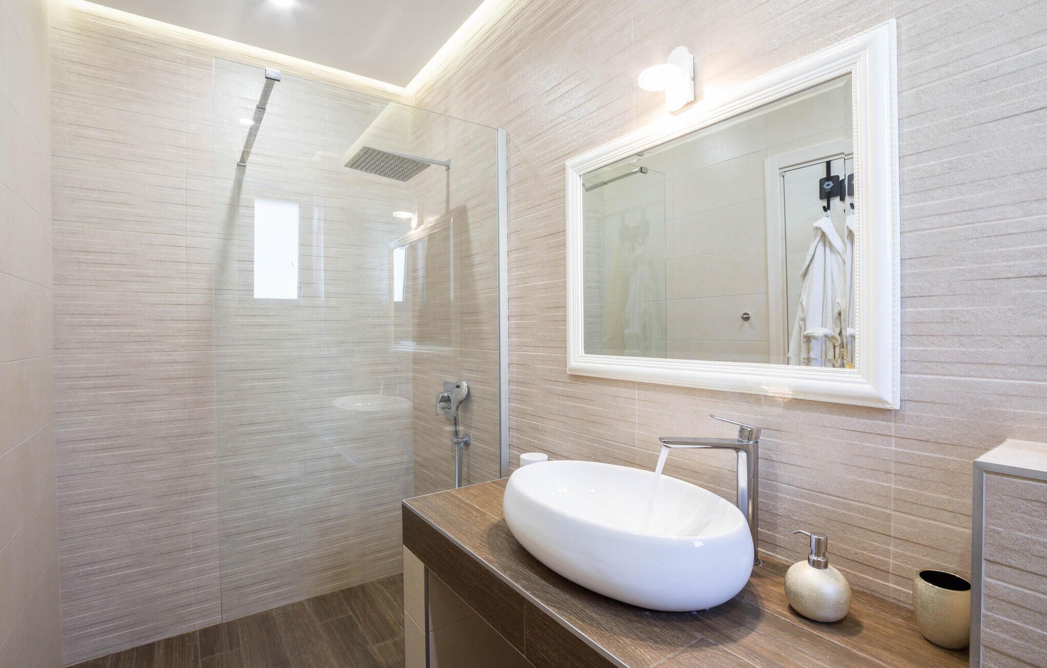A modern bathroom with a glass-enclosed shower, a large mirror, and a round sink.