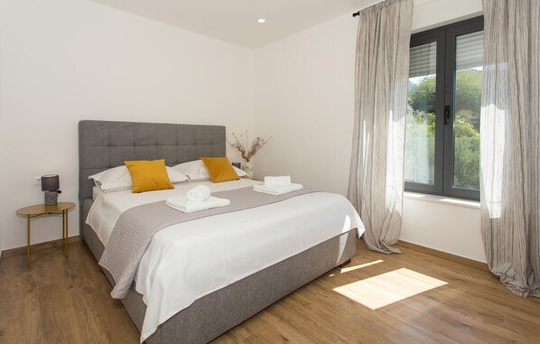 Quarto moderno com cama estofada cinza, roupa de cama branca e almofadas mostarda.