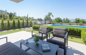 Une terrasse avec deux chaises, une table et un livre. On aperçoit une piscine au fond.